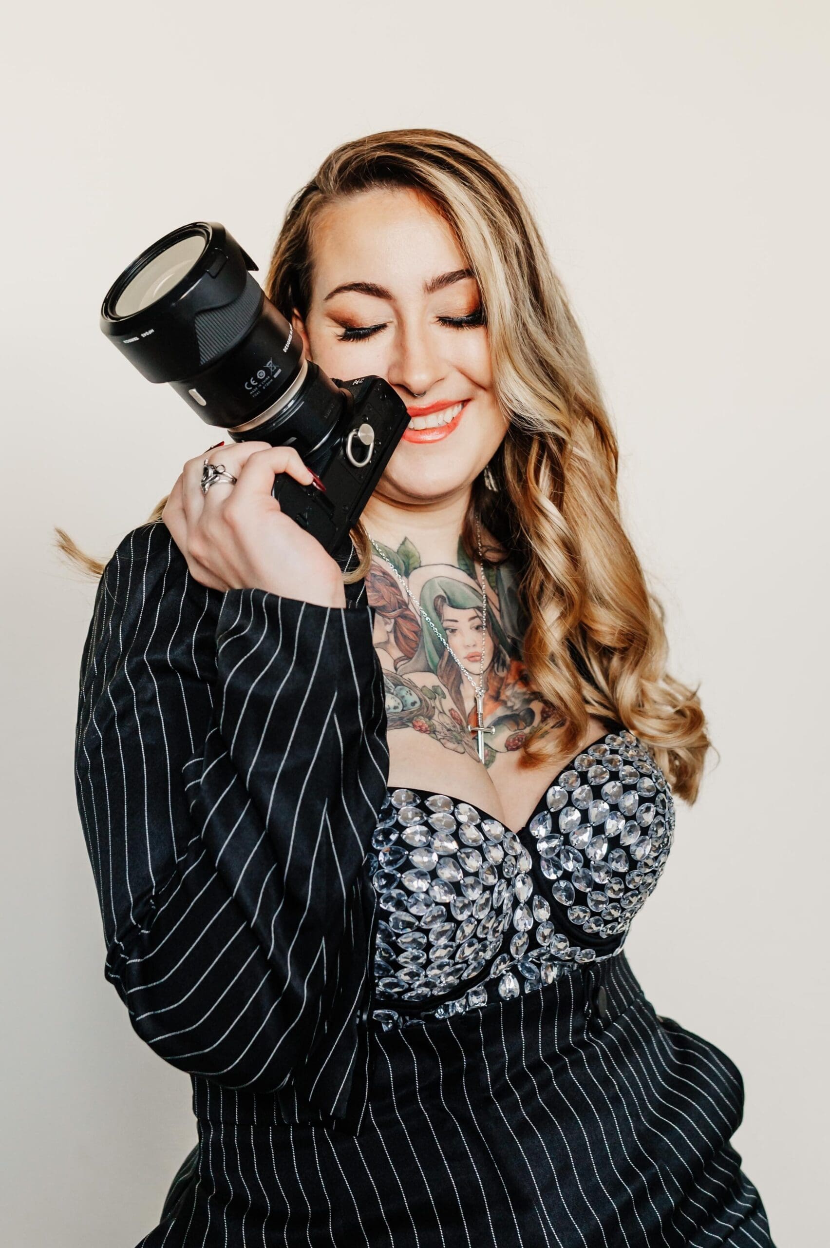 April McKeown, boudoir photographer and owner of Helios Boudoir Photography, smiling while holding her camera in a glamorous pinstripe outfit.