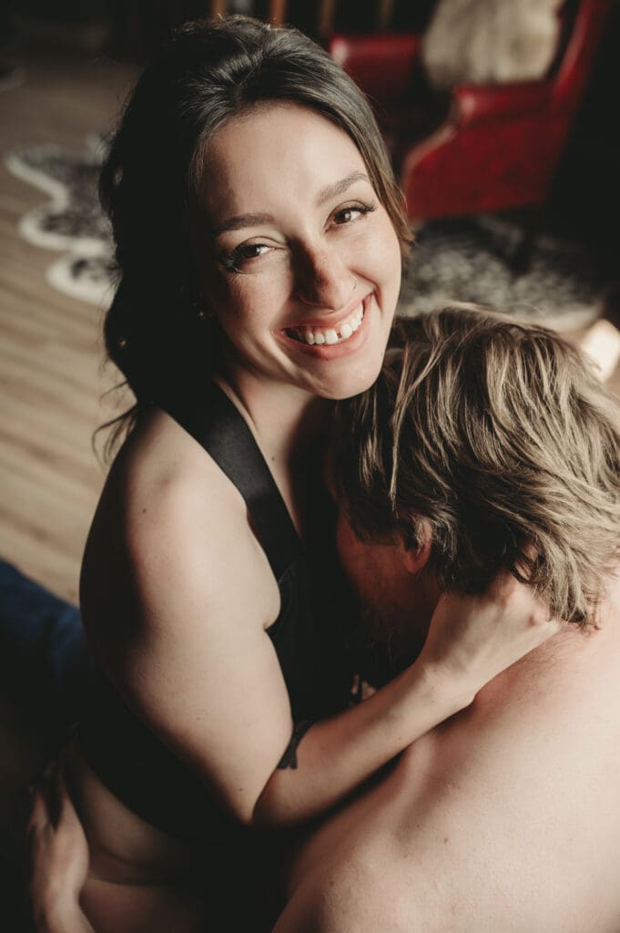 Playful and joyful moment during a couples boudoir session at Helios Boudoir Photography, showing a woman laughing and embracing her partner in a lighthearted, intimate setting.