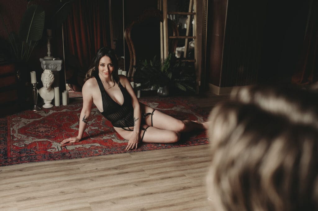 Woman in black lingerie posing confidently on a vintage rug during couples boudoir session at Helios Boudoir Photography studio in Salem, Oregon.